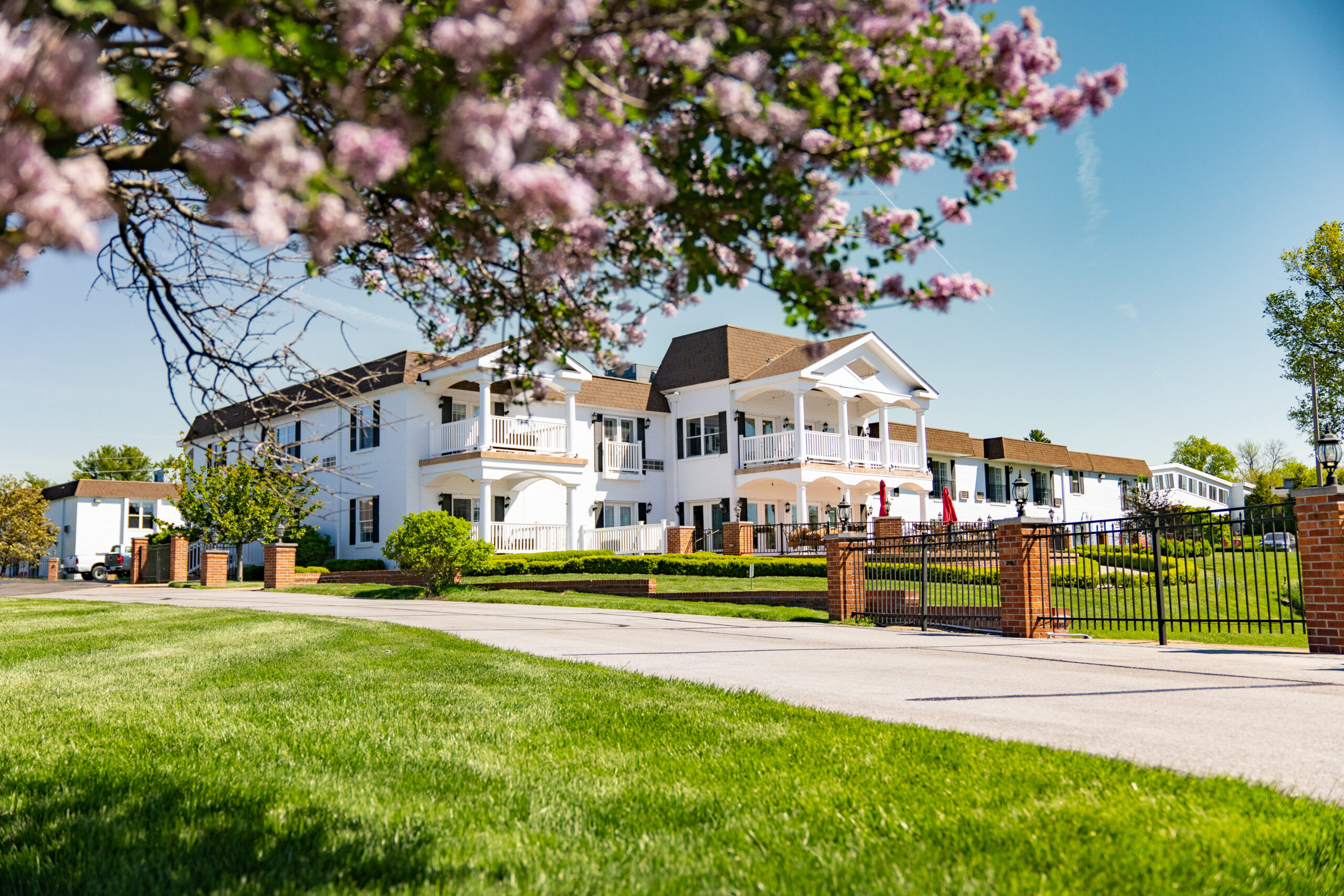 Beautiful exterior of Mari de Villa, a luxury assisted living facility near you, with blooming flowers in the foreground and a clear blue sky.
