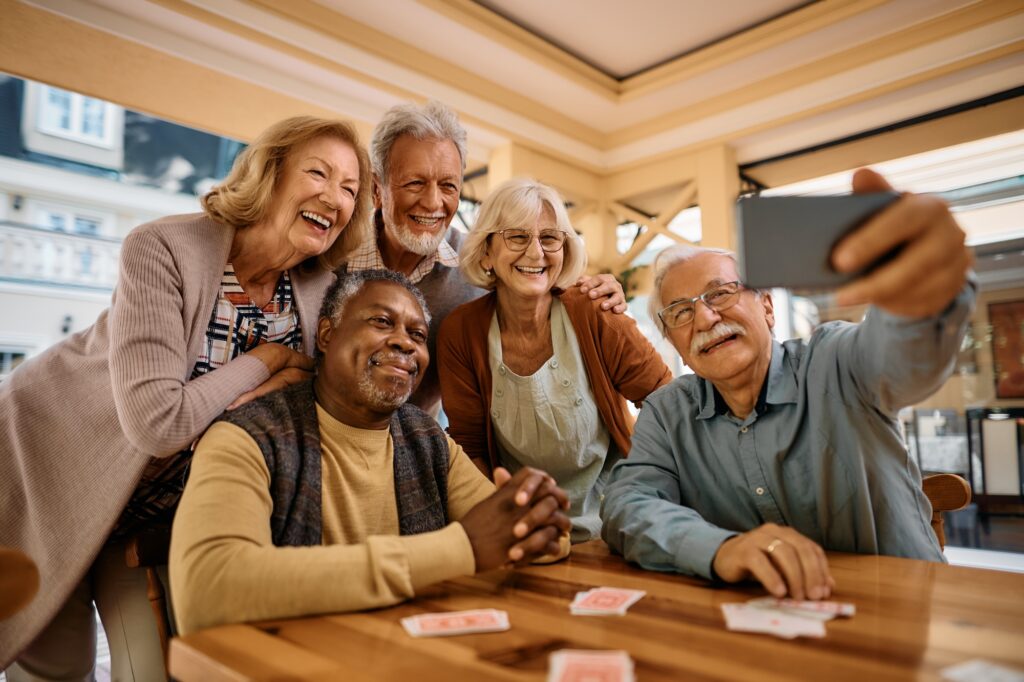 The Ultimate Guide to 55+ Communities Near St. Louis: Discover Elevated Senior Living at Mari de Villa 2 Friends laughing and taking a selfie while playing cards, highlighting the social connections and joy found in 55+ communities near me like Mari de Villa.