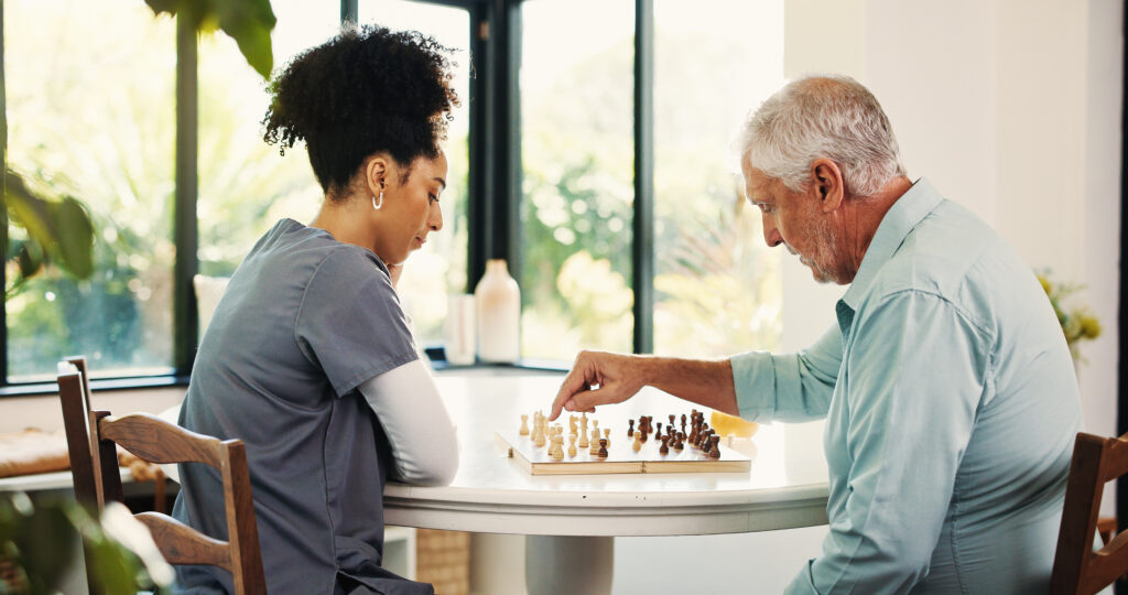 Skilled nursing caregiver providing personalized support while playing chess with a senior resident during recovery.