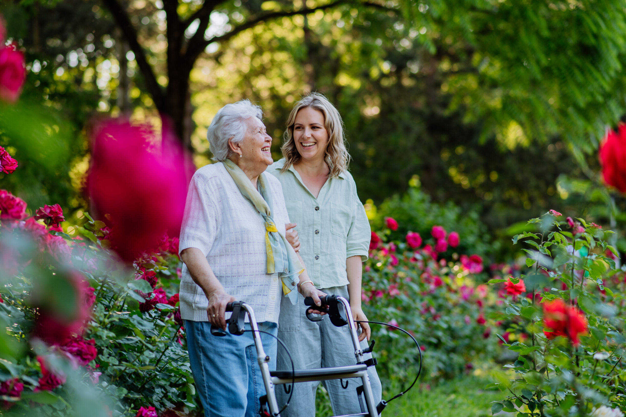 Skilled nursing support helping an older woman walk safely with a walker outdoors during short-term rehabilitation.
