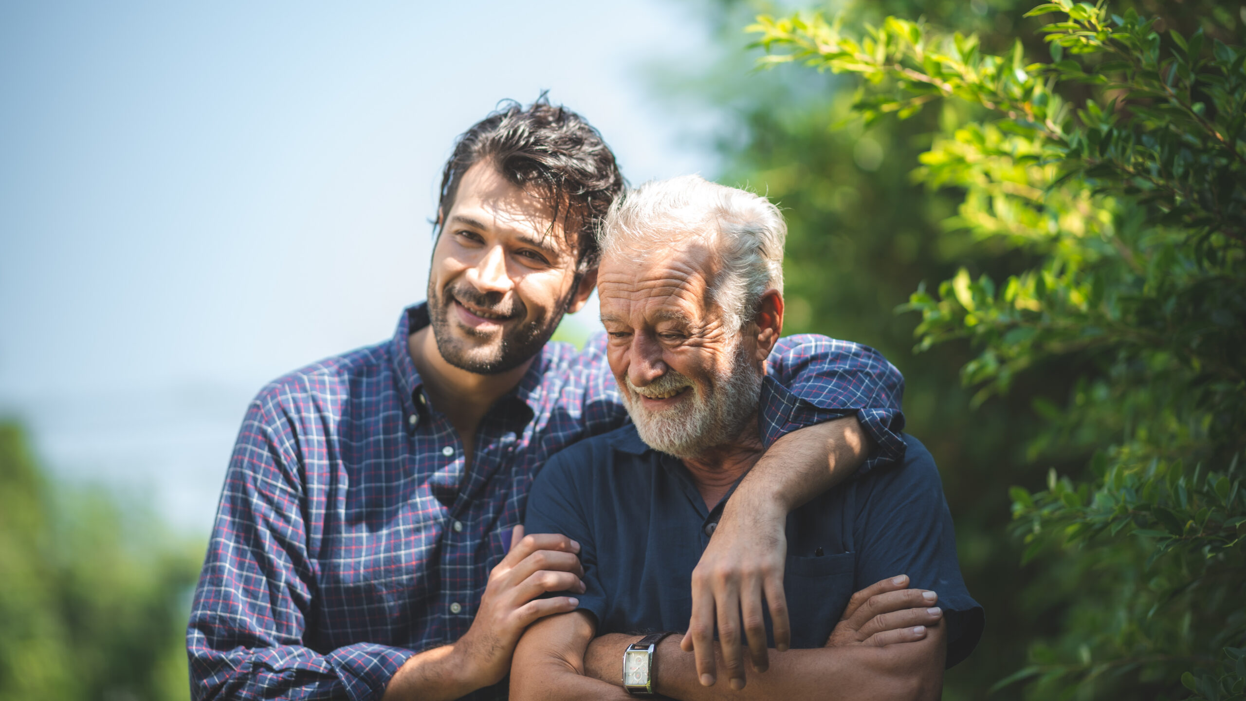 Adult son with his arm around his smiling father, representing caregiver support for aging parents